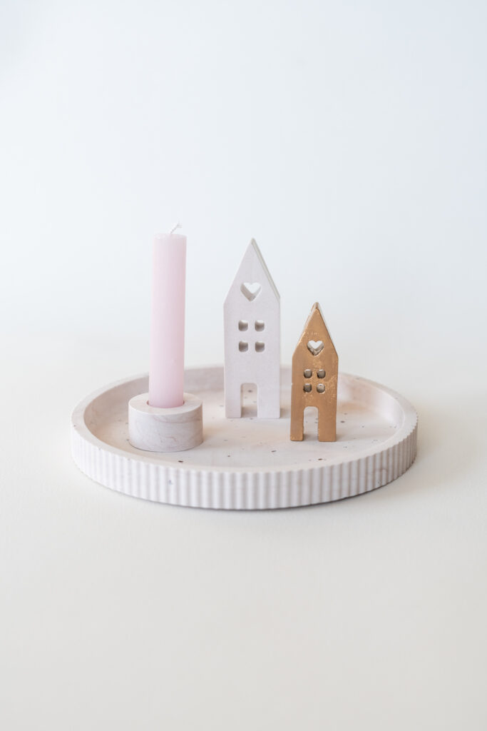 Ronde geribbelde Jesmonite kaarsenhouder met een roze kaars en twee kersthuisjes in wit en naturel